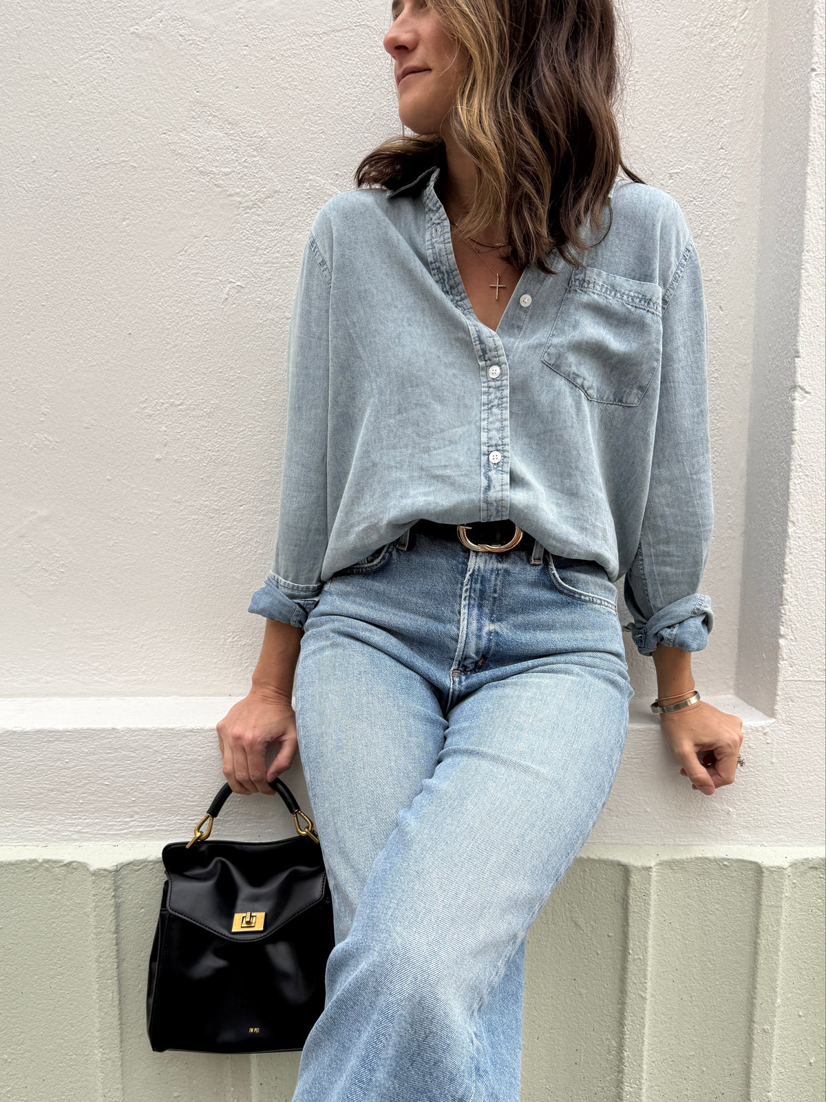Person wearing a light blue denim outfit with a black bag on a white background